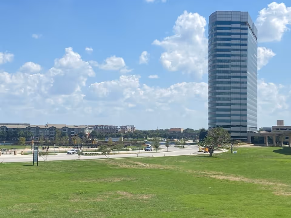 Wide exterior view of a tall modern building with green lawn and blue sky.