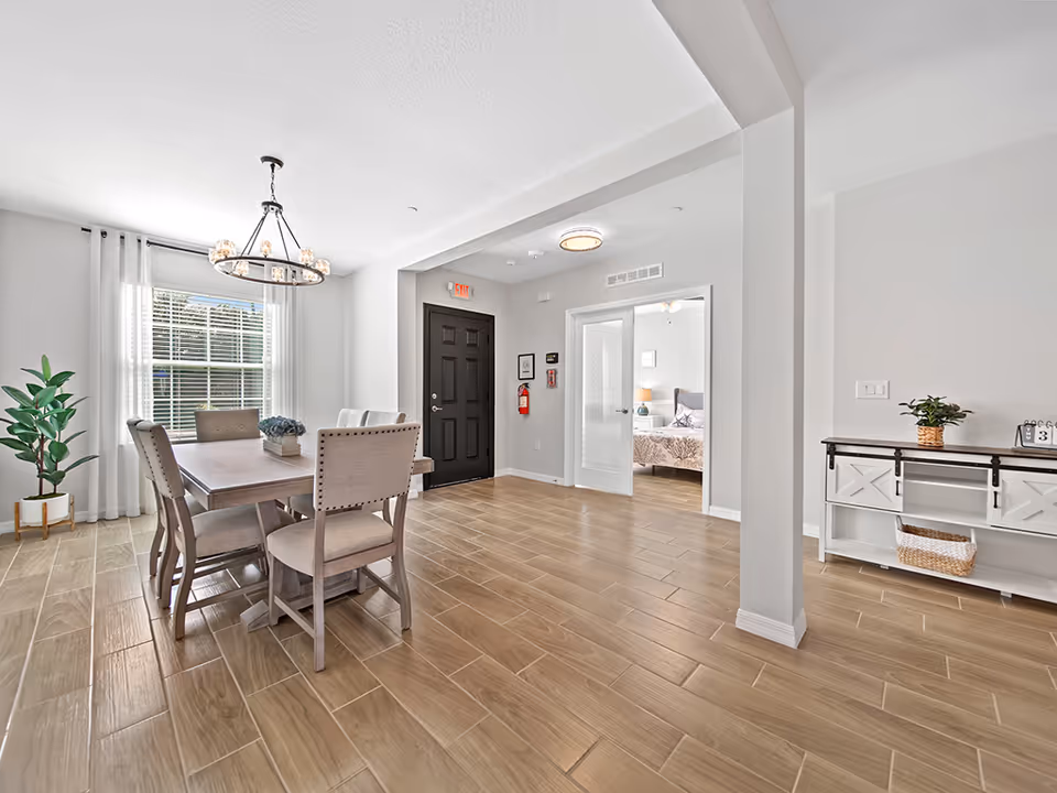 Interior dining area with a wooden table, chairs, chandelier, and an adjacent bedroom doorway.