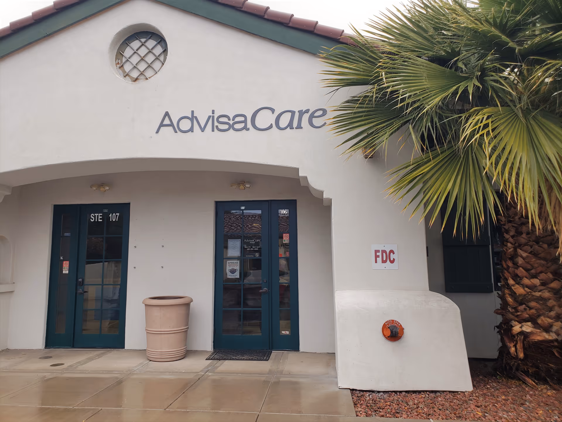 Exterior of AdvisaCare facility with double doors, palm tree, and signage.