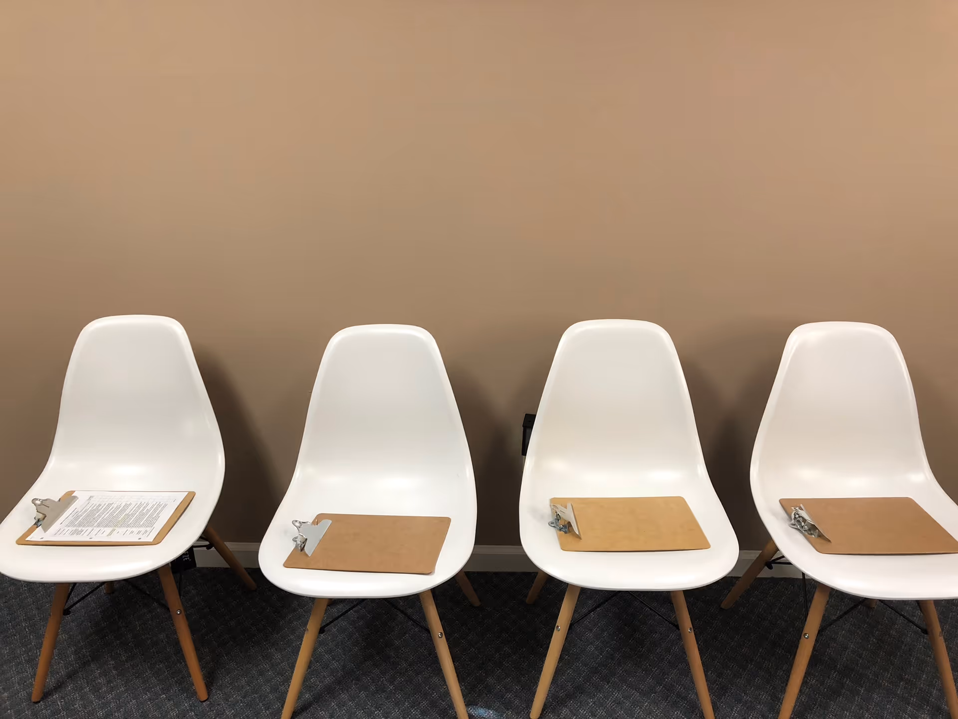 Row of white modern chairs with clipboards on seats against brown wall