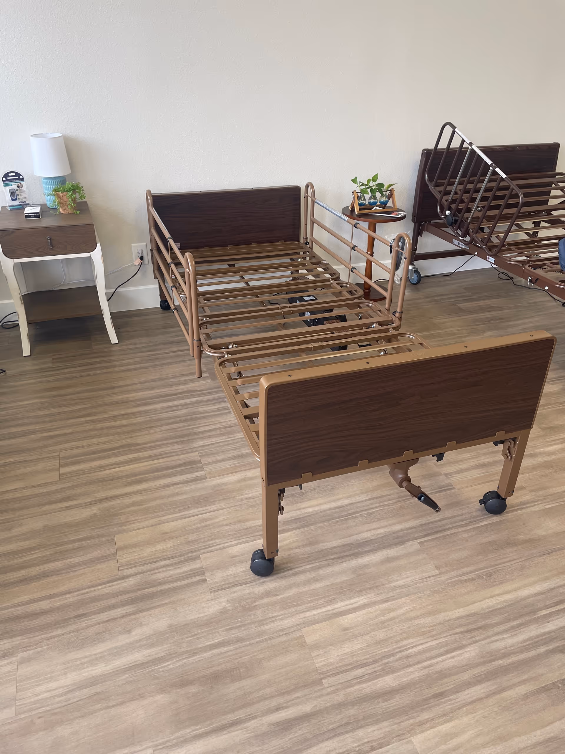 Two brown adjustable hospital beds with rails in a clean senior living bedroom.