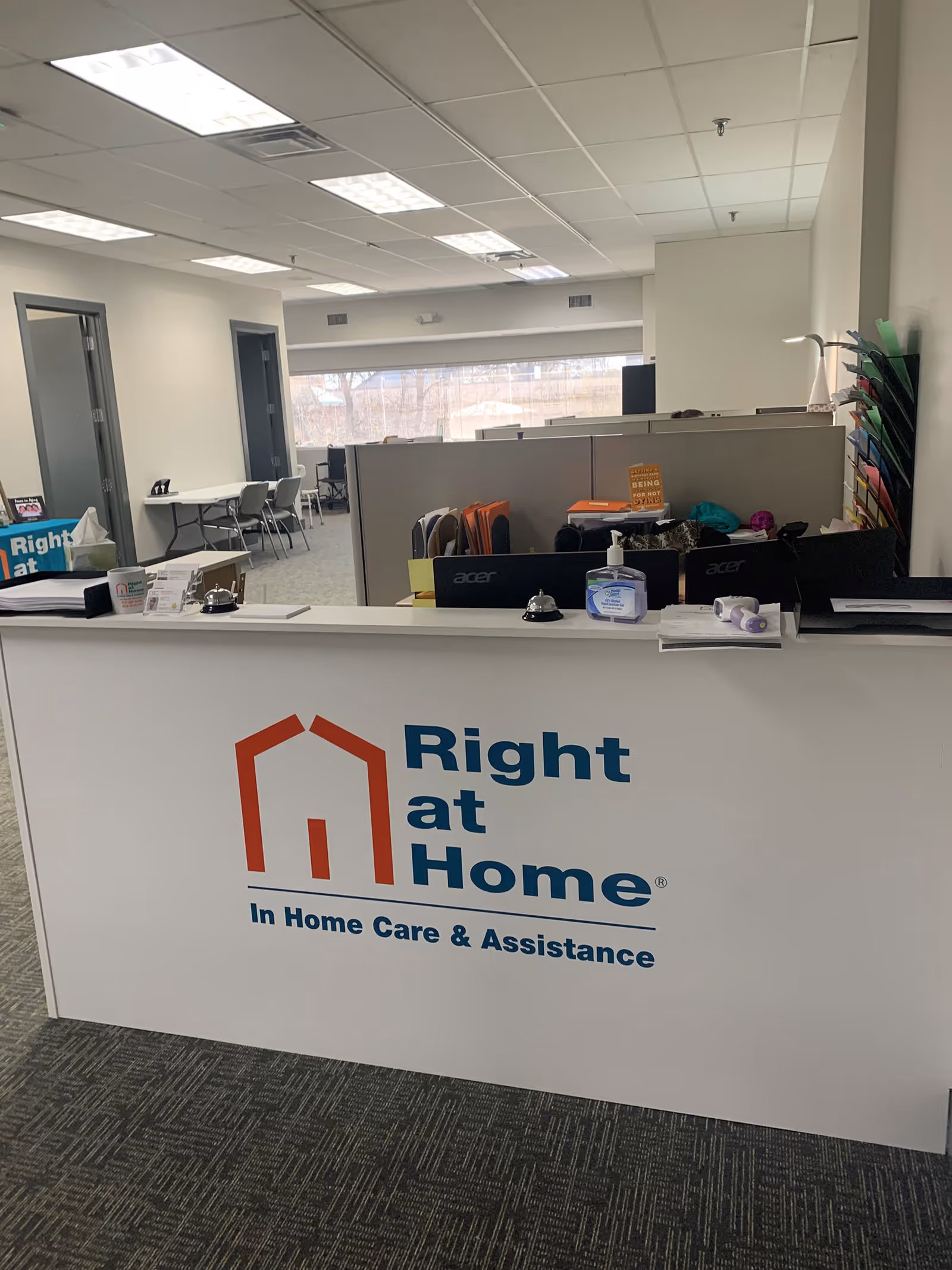 Reception desk with Right at Home logo and office cubicles in a bright indoor lobby.