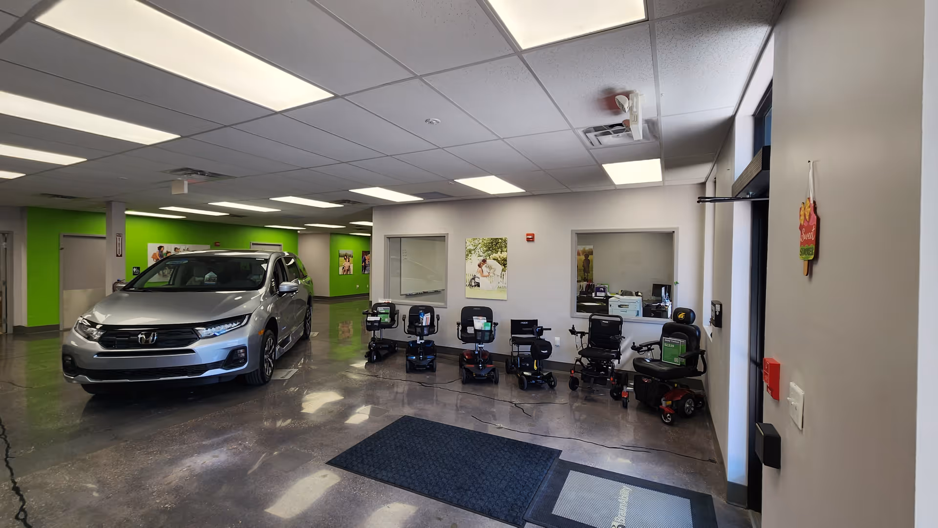 Inside a MobilityWorks showroom, a silver SUV sits beside several mobility scooters and wheelchairs.