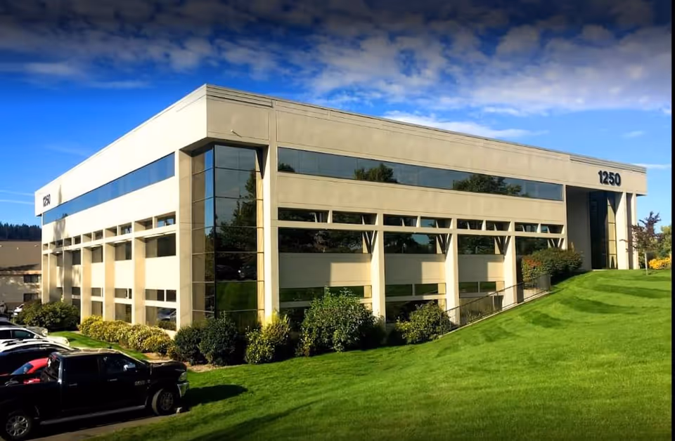 Modern beige building with large glass windows, green lawn, and parked cars along the front.