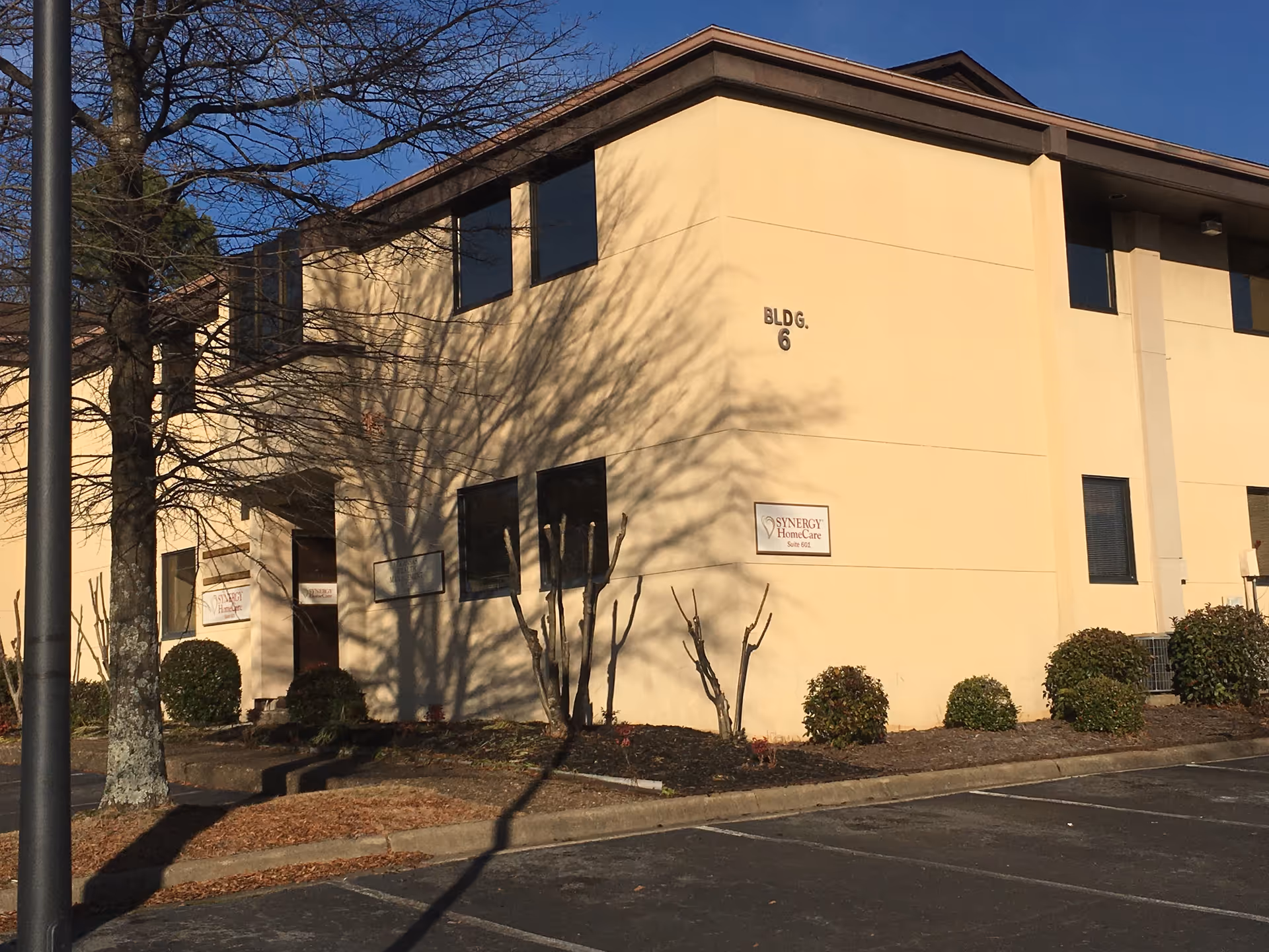 Two-story beige senior care building with windows, landscaping, and a parking lot in front.