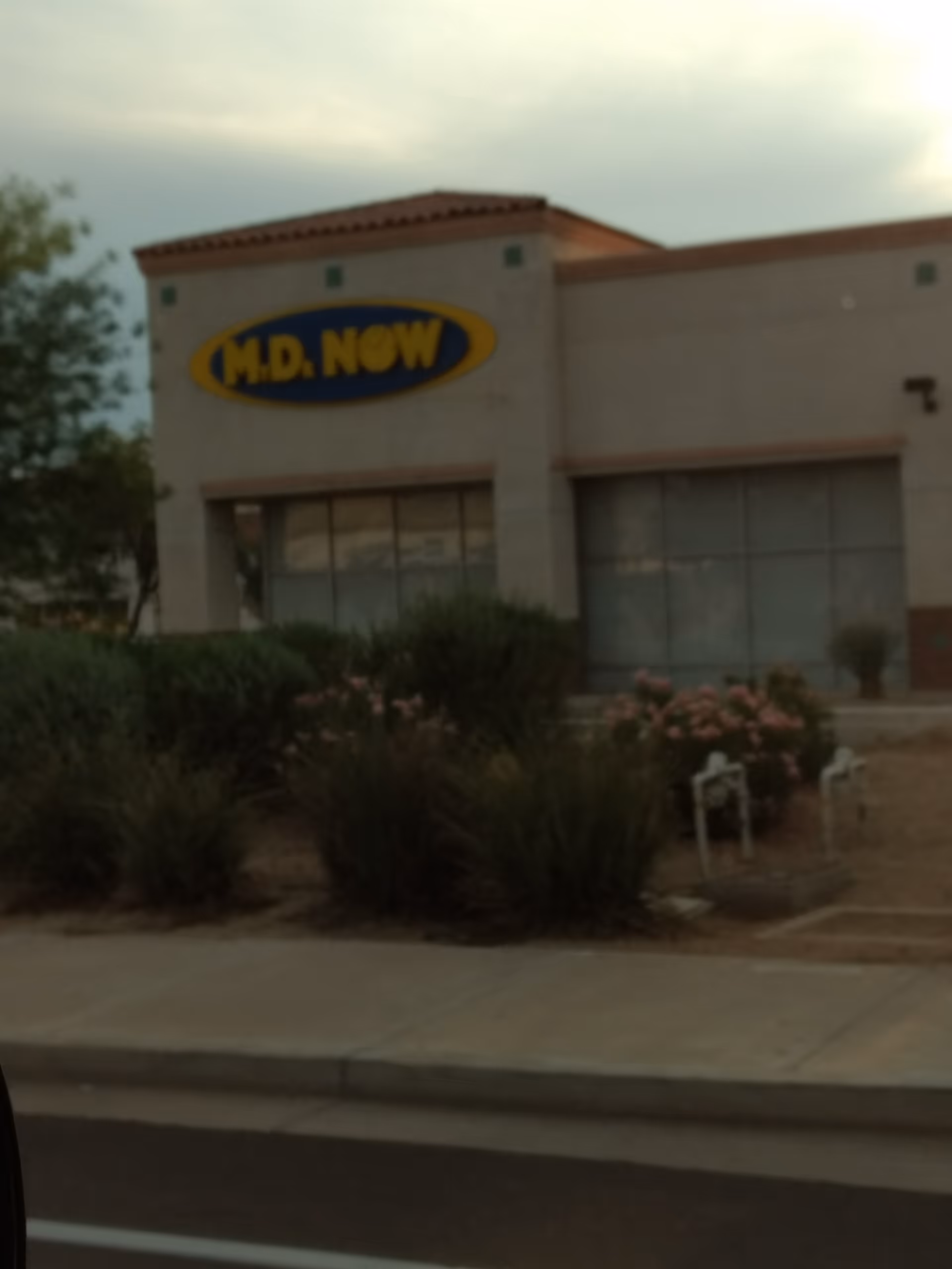 Exterior view of a facility front with MD NOW sign and landscaped shrubs.