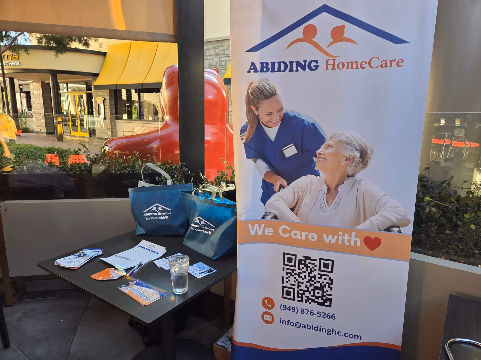 Outdoor promotional display for Abiding Home Care with brochures on a table and banner.