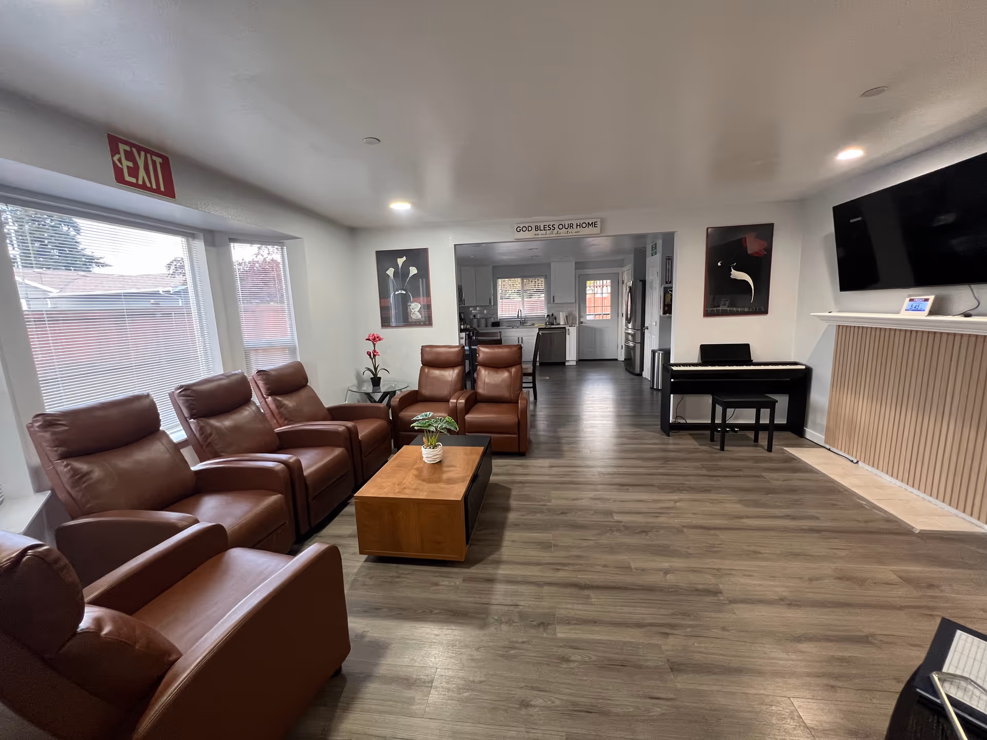 Bright living area with leather recliners, a coffee table, piano, and a visible kitchen in back.