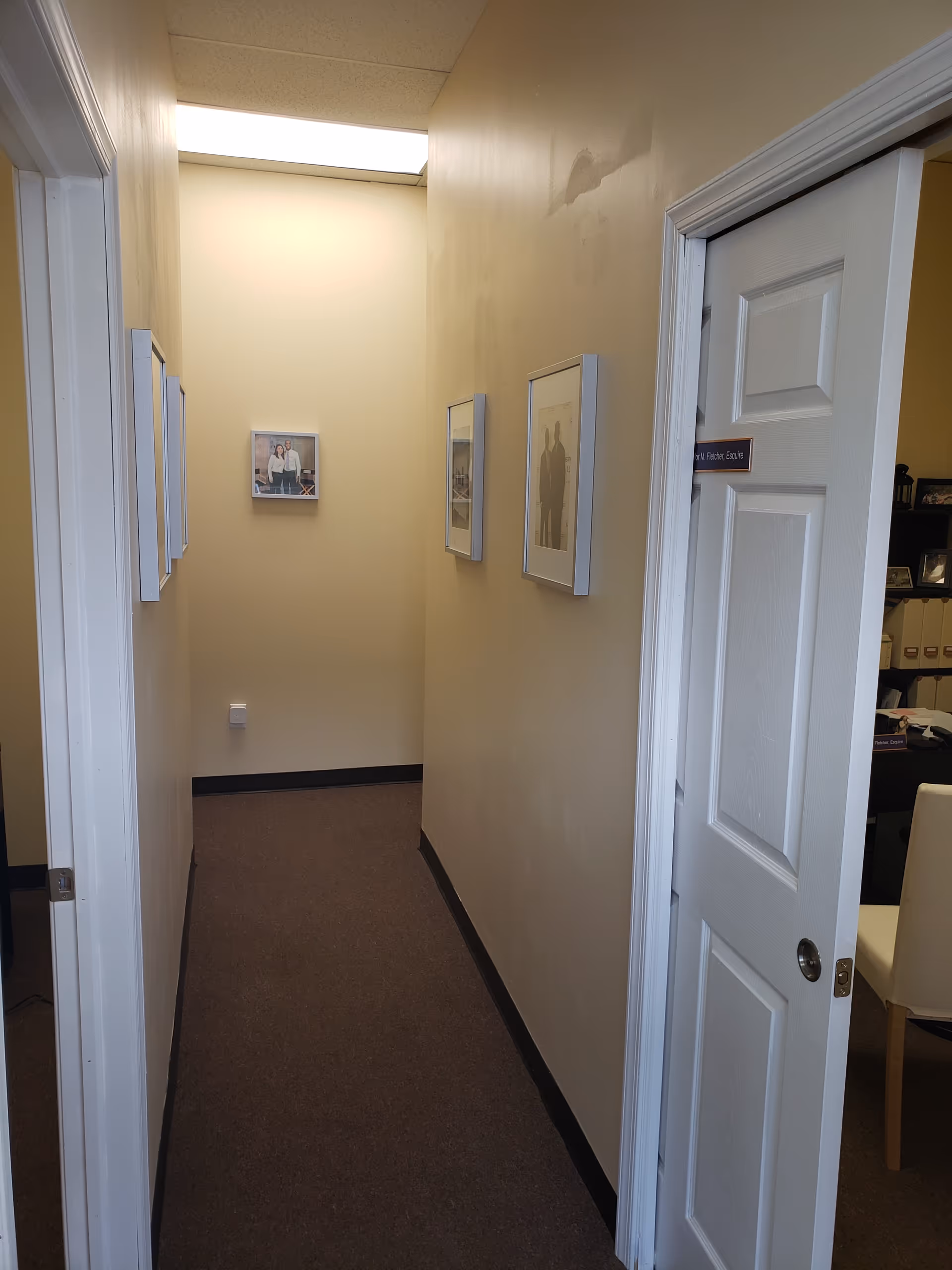 Narrow beige hallway with framed photos and an open office door.
