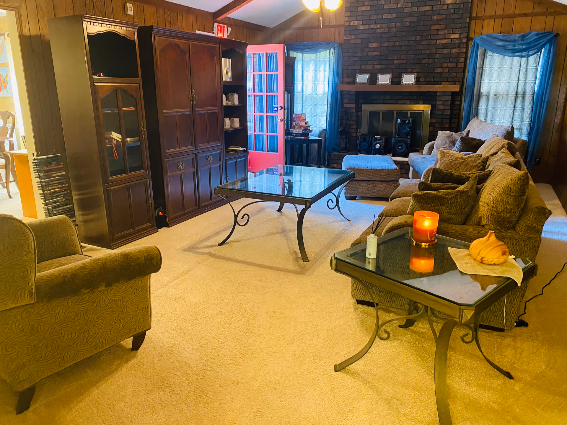 Cozy living room with brown couches, glass tables, a brick fireplace, and blue curtains.