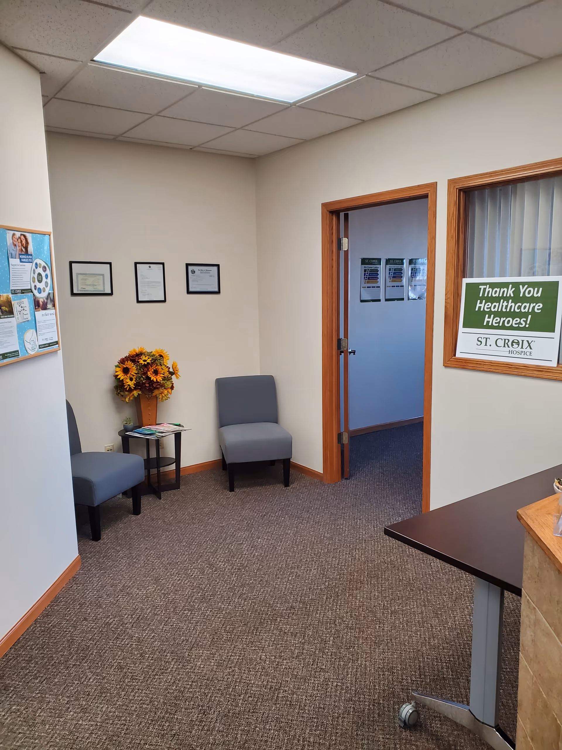 A small hospice waiting area with two blue chairs and a side table near a doorway