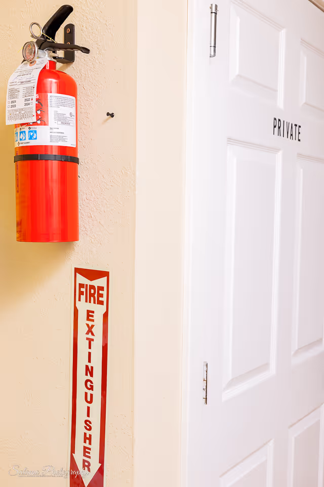 Red fire extinguisher and a private door along a beige interior hallway.