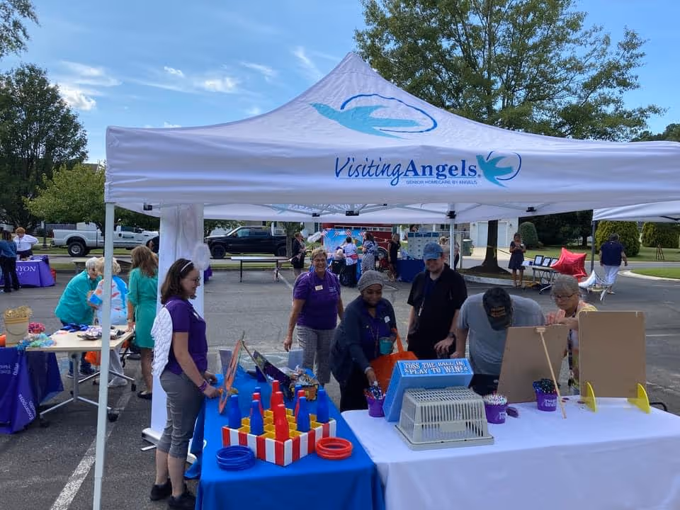 Outdoor event under a Visiting Angels tent with volunteers and attendees at tables.
