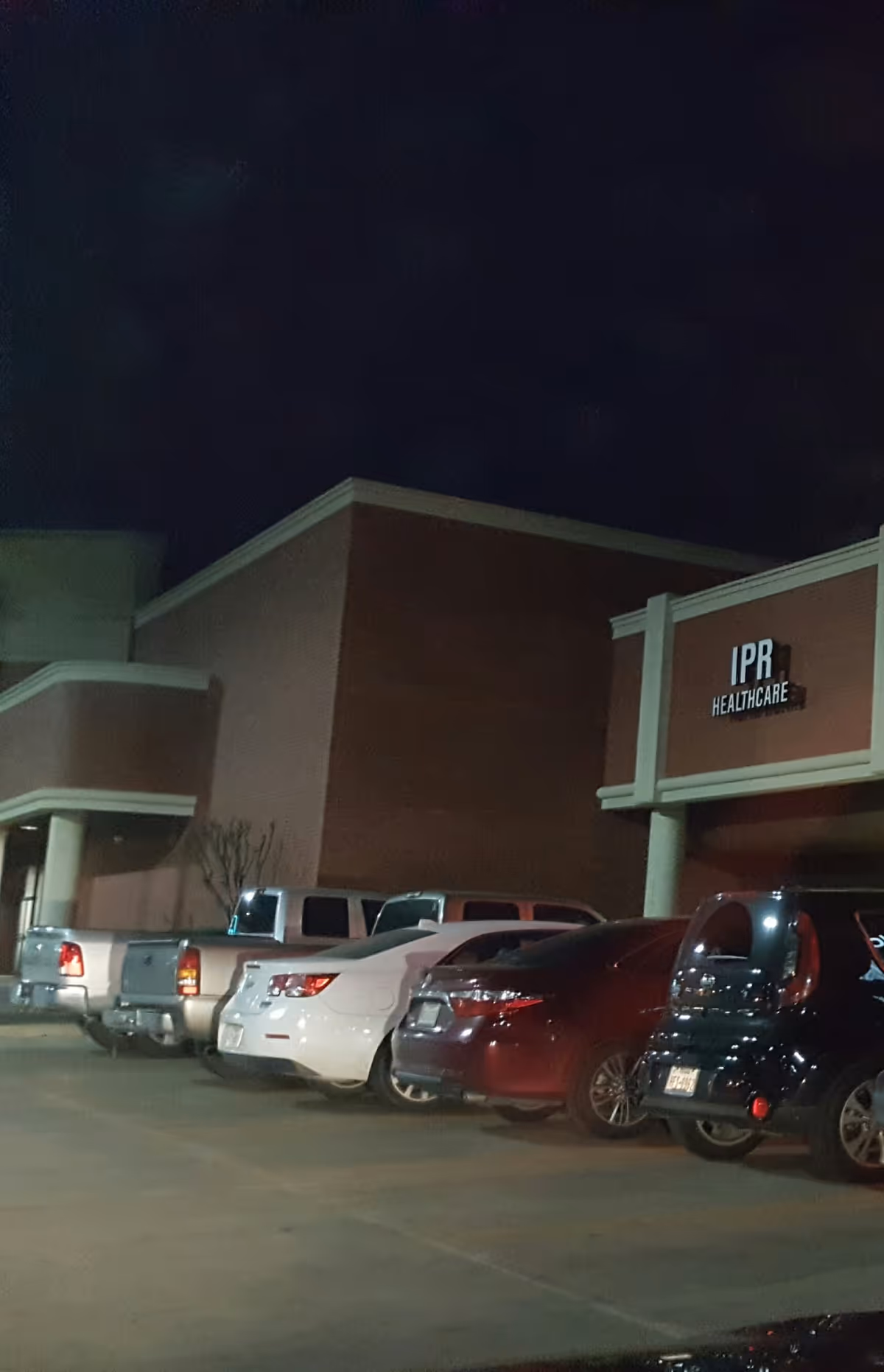 Night exterior of IPR Healthcare building with parked cars in front.