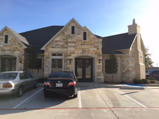 Stone-front facility exterior with arched entry, parked cars, and a clear blue sky.
