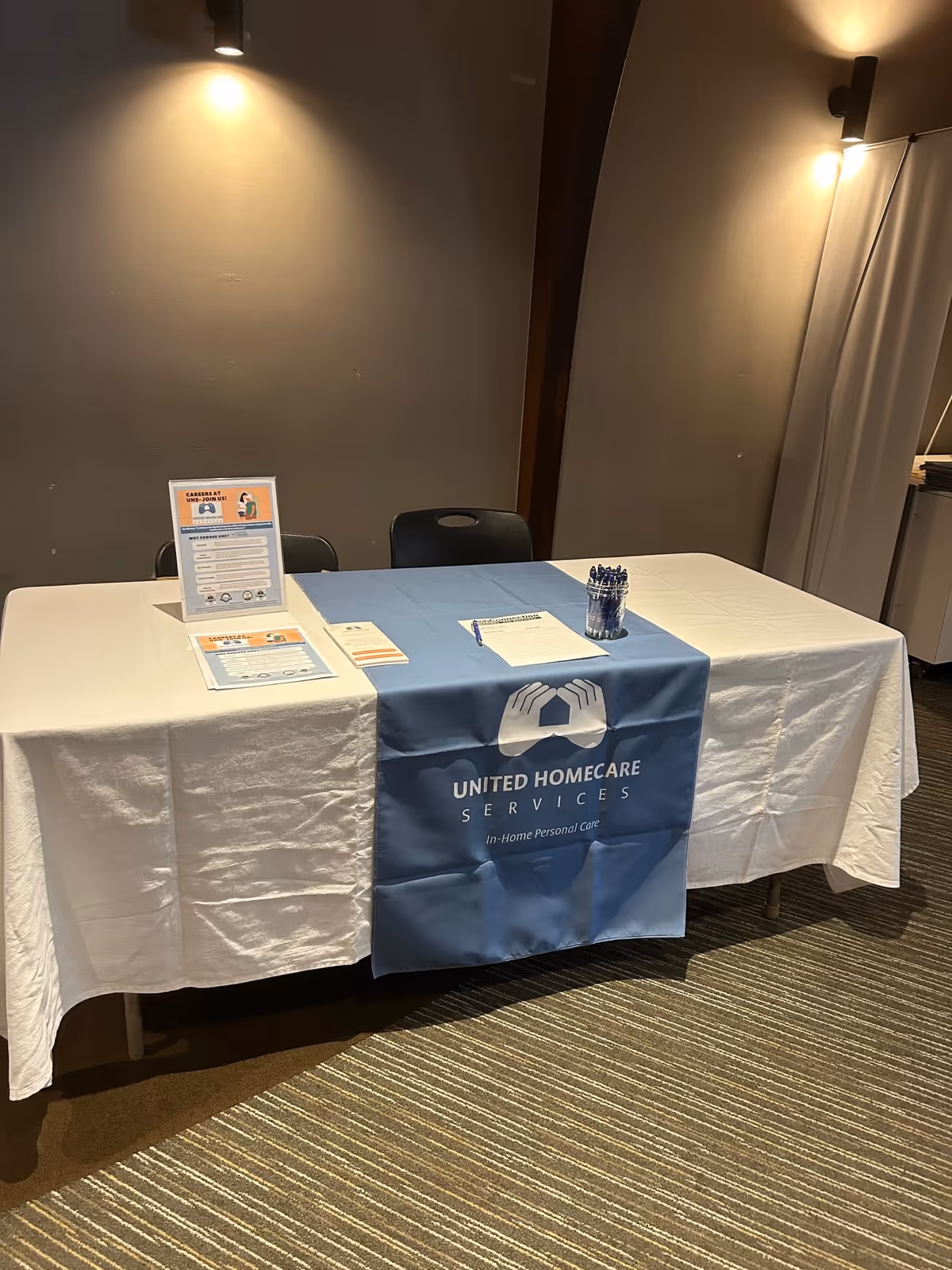 Registration table with United Homecare Services banner in a dim indoor room.