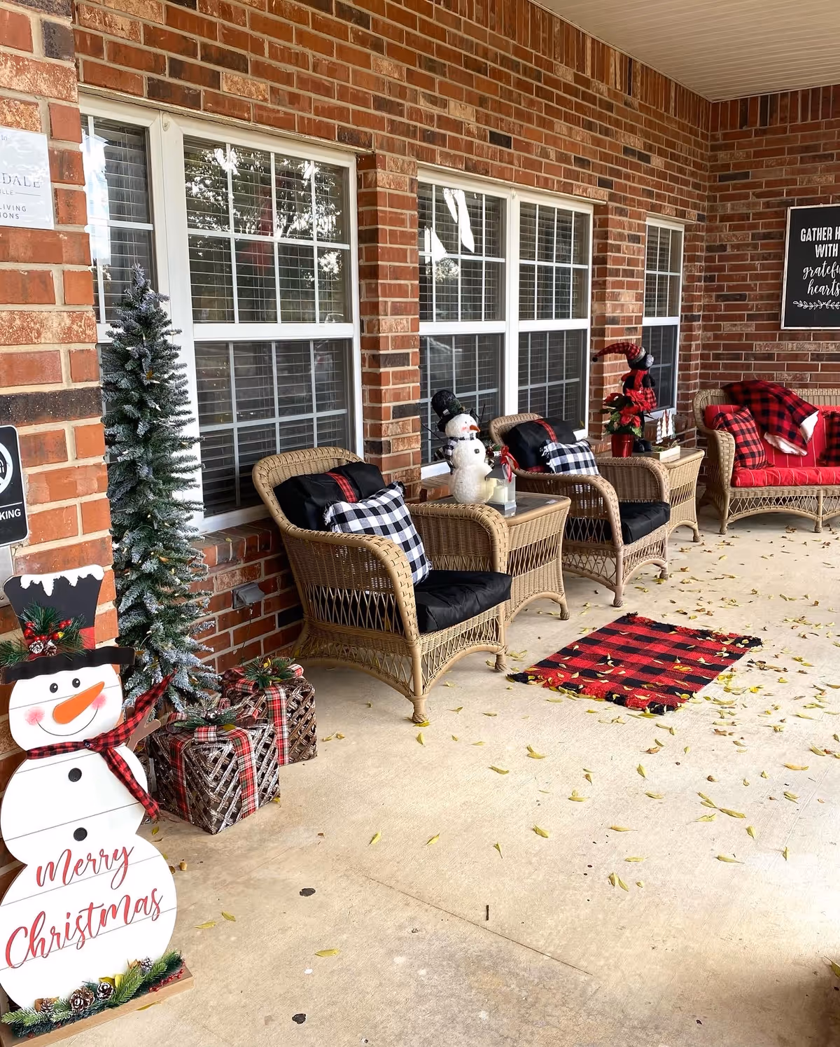 Outdoor brick porch with wicker chairs, holiday decor, snowman, and Christmas-themed accents.