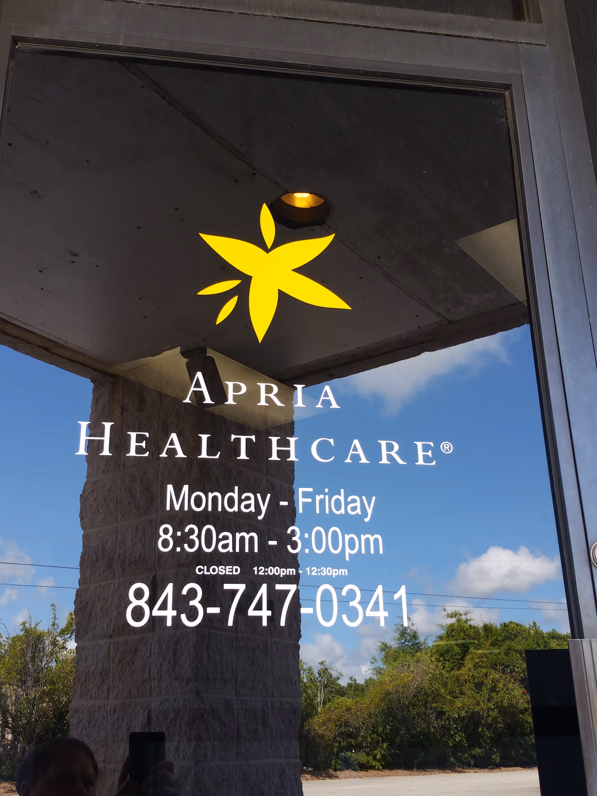 Glass storefront entrance with Apria Healthcare logo and hours on the door.