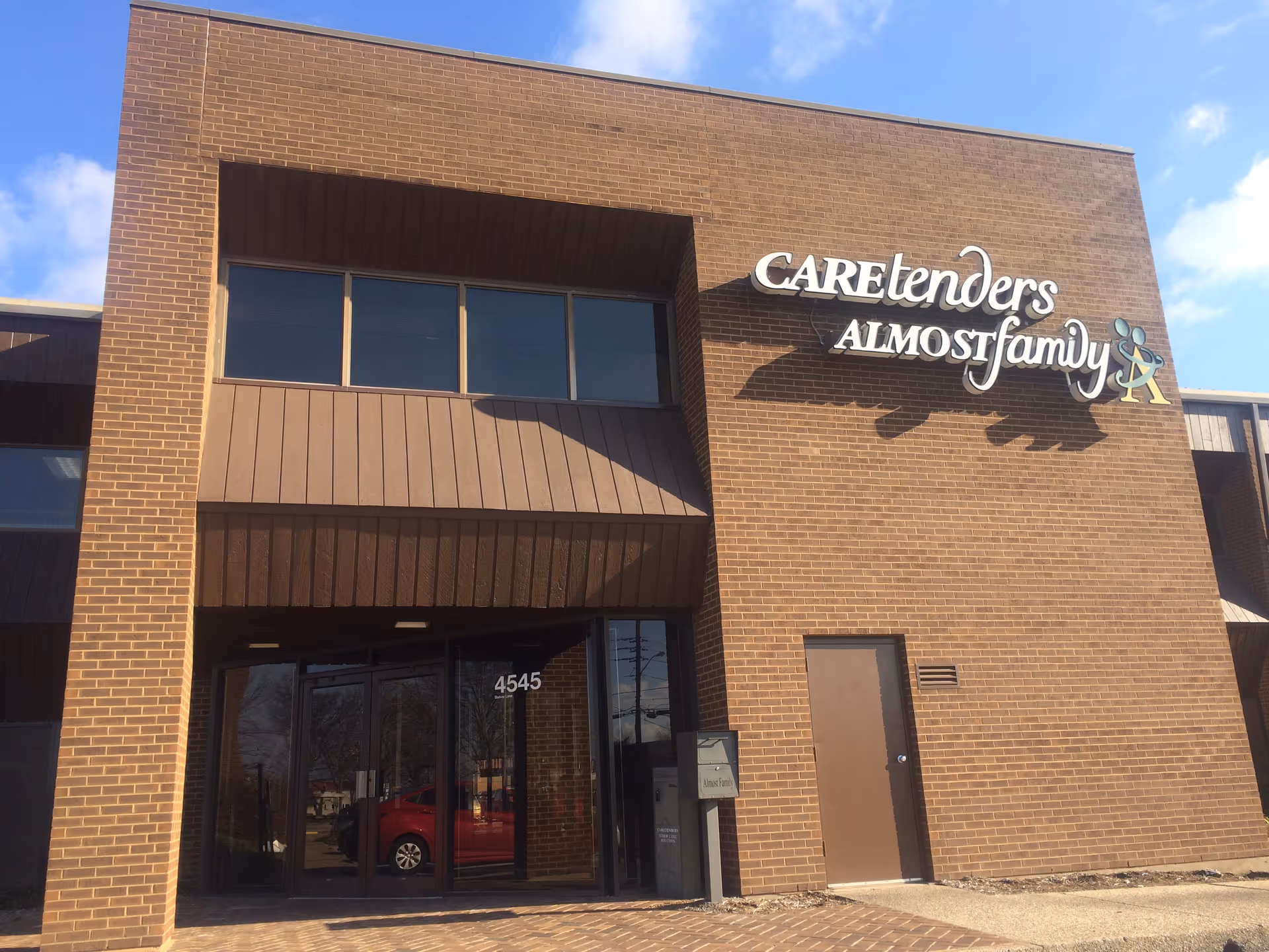 Brick senior living facility with Caretenders Almost Family sign and glass entrance.