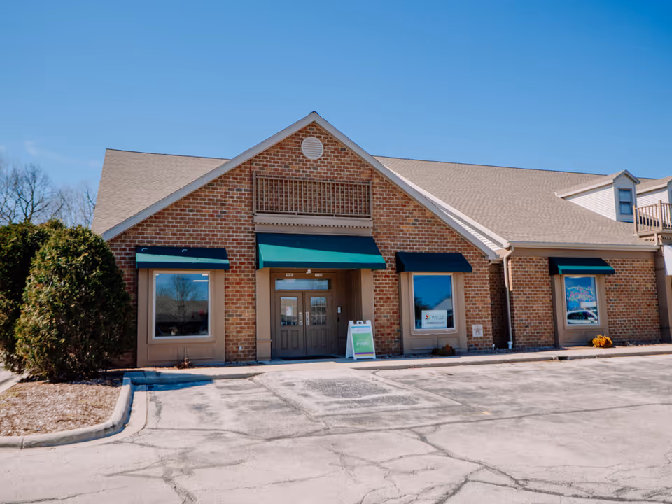 Front view of a brick facility with green awnings and a parking lot.