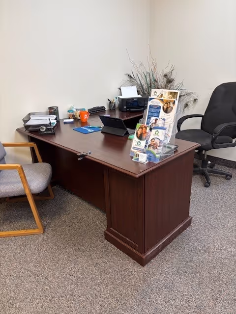 A wooden desk with chairs, brochures, and office equipment in a small staff office.