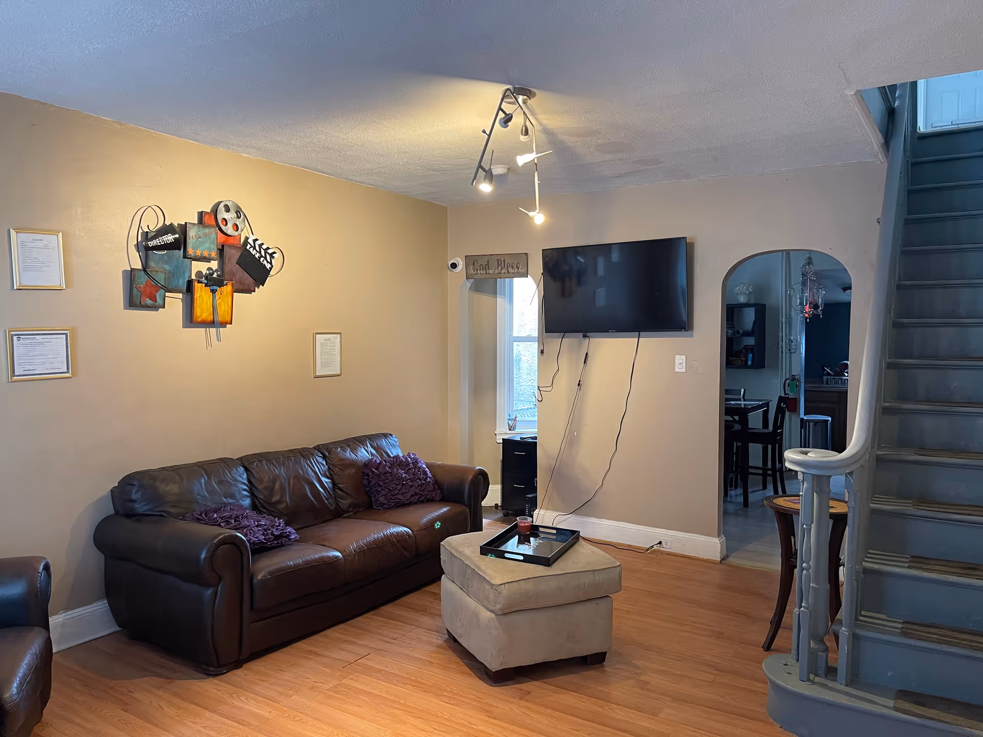 Cozy living room with leather sofa, ottoman, wall-mounted TV, and curved staircase.