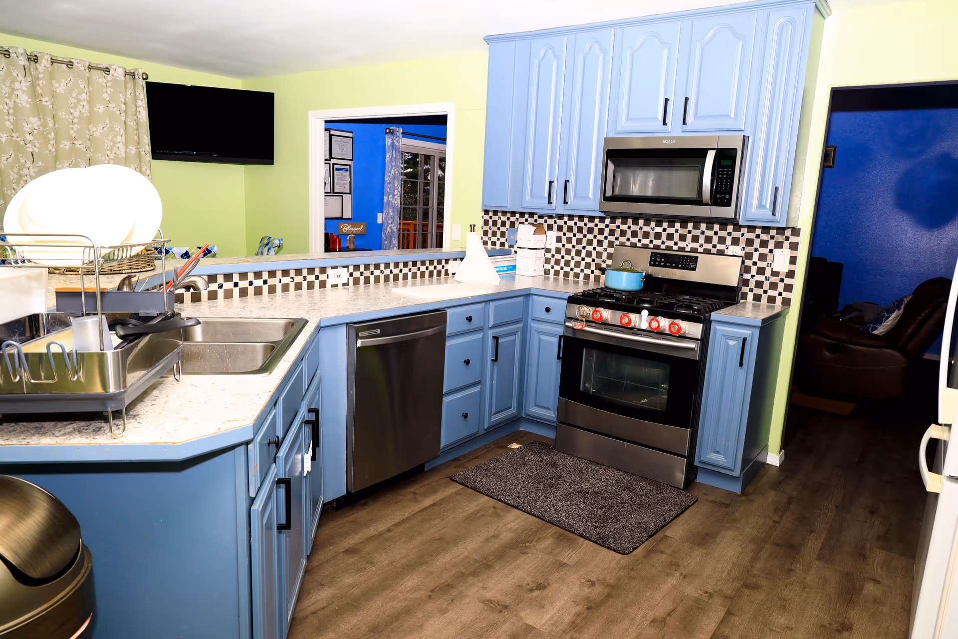 Bright blue kitchen with stainless appliances, tile backsplash, and doorway to a living area.