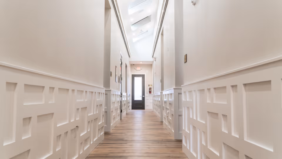 Bright white hallway with paneled walls and a dark door at the end.