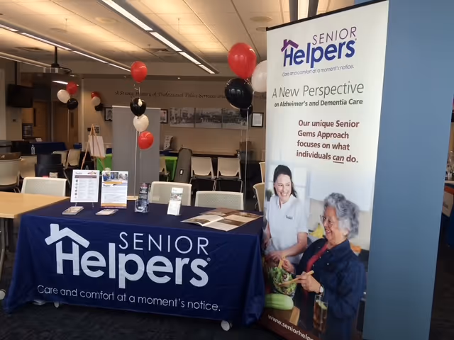 Promotional Senior Helpers booth inside a facility, with a blue banner, roll-up banner, and balloons.