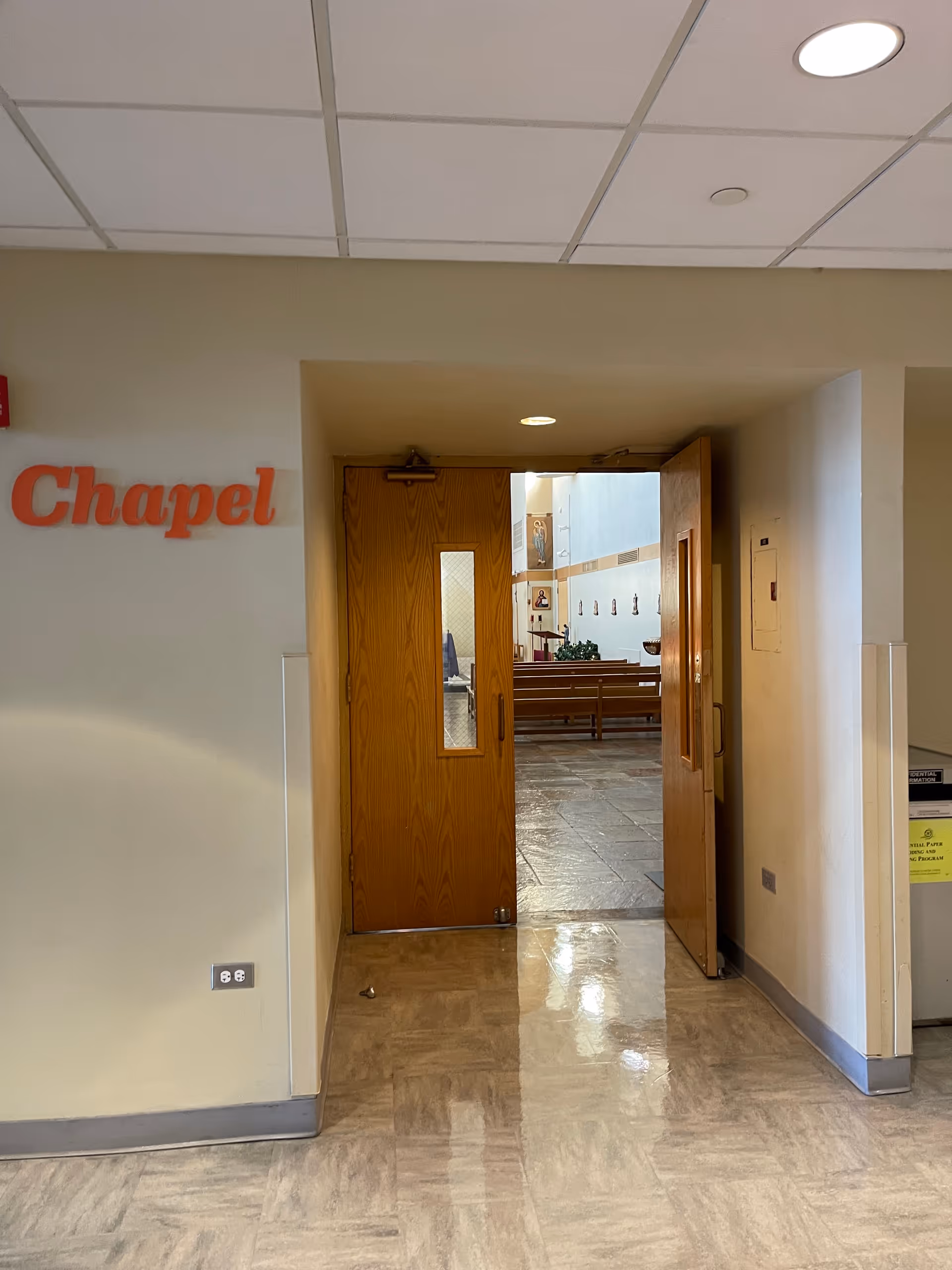 Double wooden doors open to a chapel with pews visible from a hospital corridor.