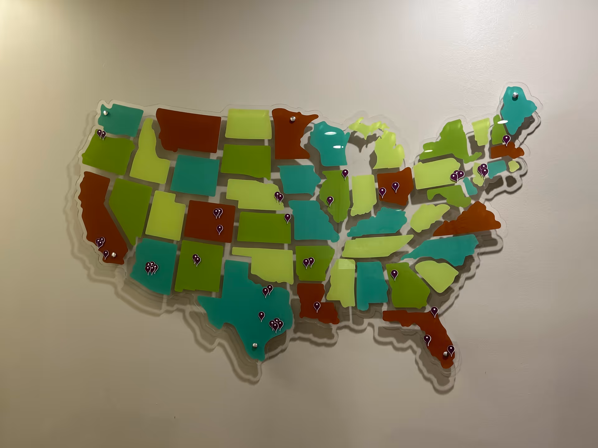 A colorful United States map wall display with pins on a beige interior wall.