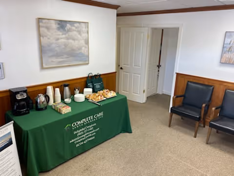 Green tablecloth refreshment table with coffee urns, cups, and pastries in a small waiting area.