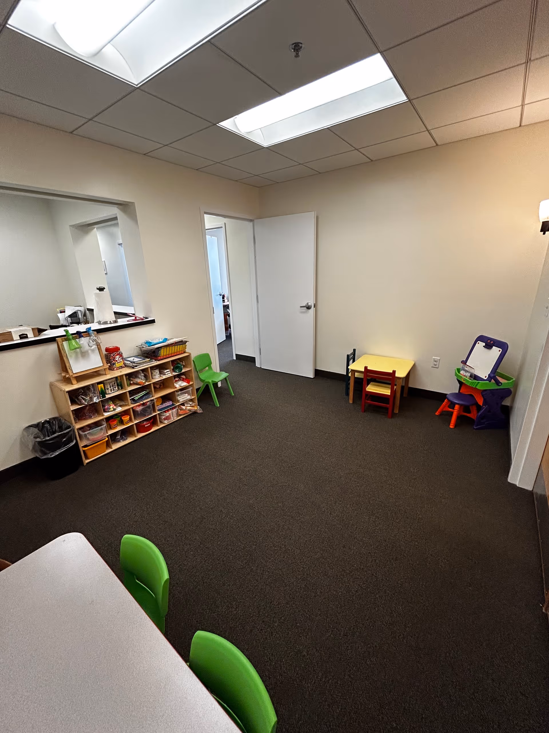 An interior sensory gym with toy shelves, small tables, and bright ceiling lights.