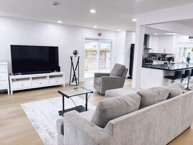 Open-concept living room at Cristina Home Care with gray sofa, TV, and kitchen island.