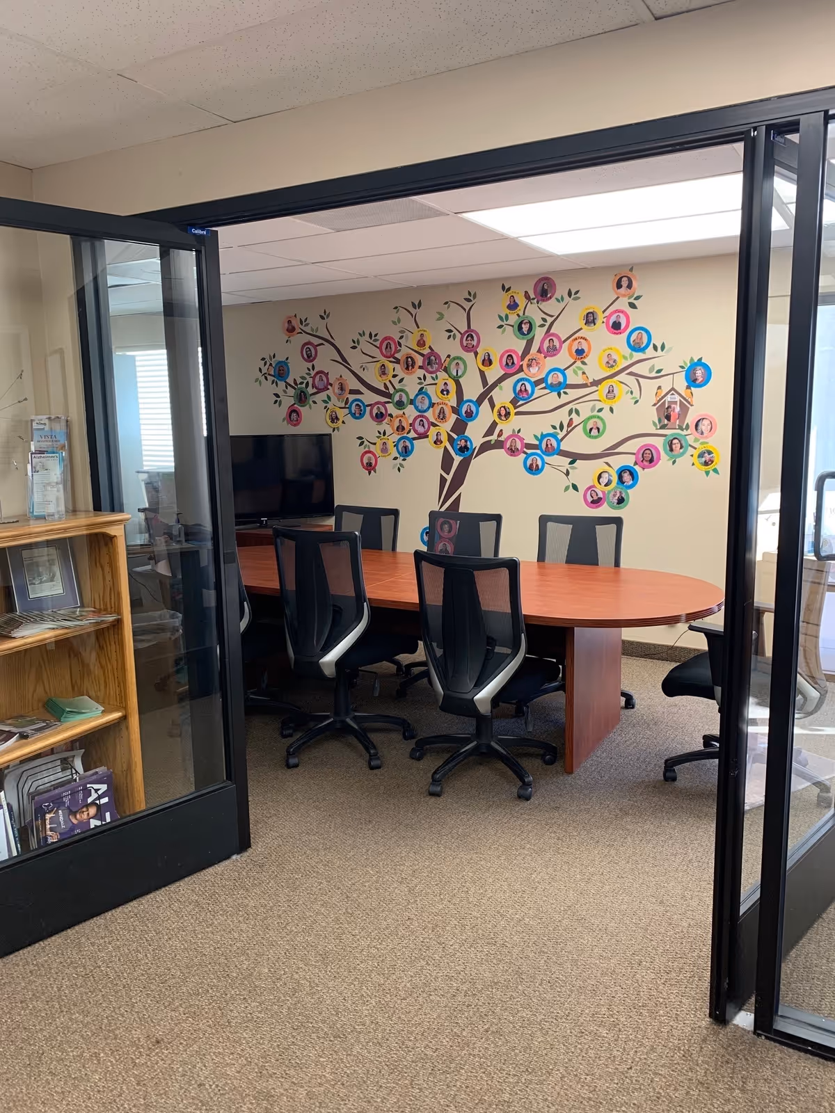 Interior conference room with round wooden table, black chairs, and colorful tree mural.