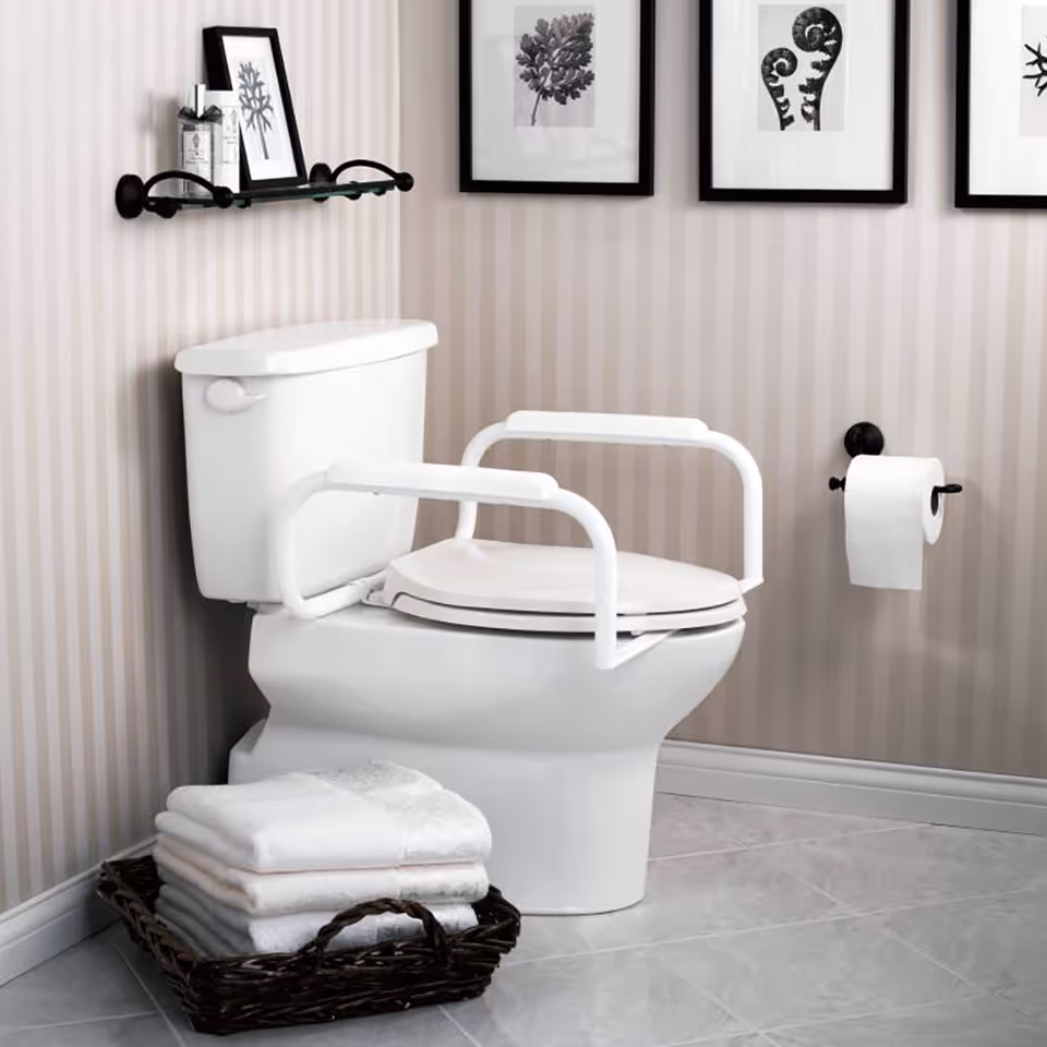 A white toilet with safety rails in a striped bathroom, basket of towels.