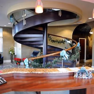 Spiral staircase in a modern, warmly lit lobby with curved railing and plants.