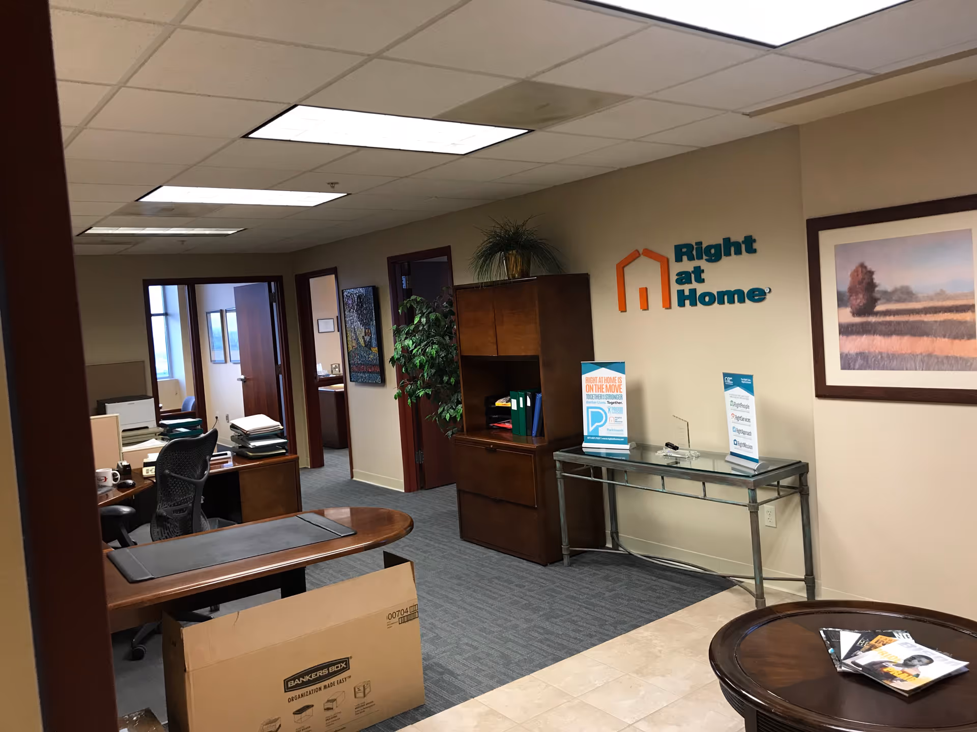 Office lobby of Right at Home with desks, cabinets, plants, and an interior logo on wall.