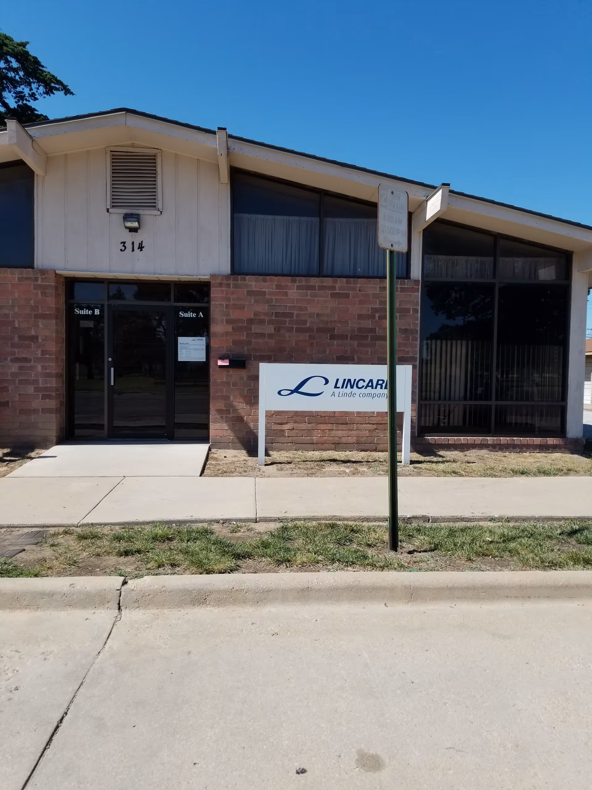 Front view of a LINCARE facility with brick exterior, glass doors, and a sidewalk.
