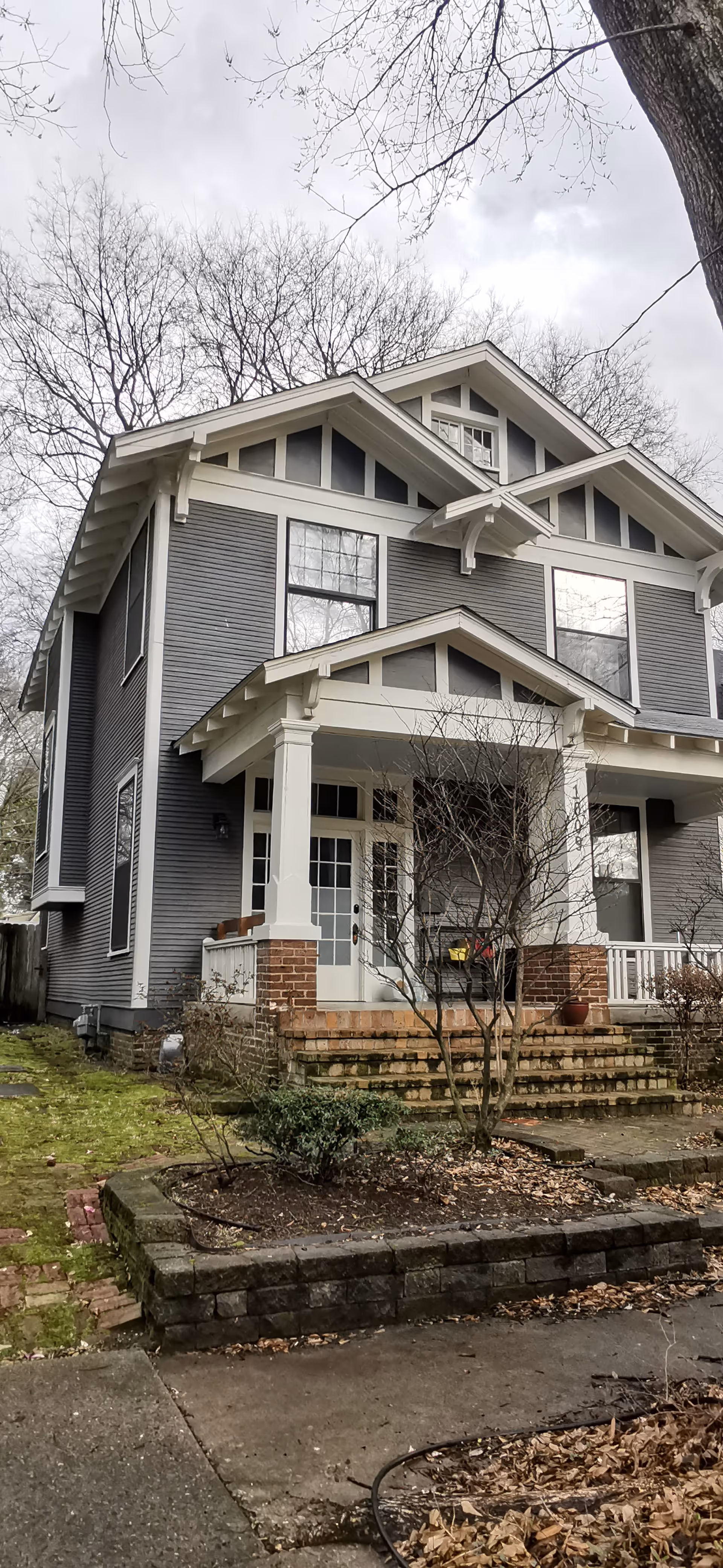 Two-story gray house with a front porch, brick steps, and leafless trees.
