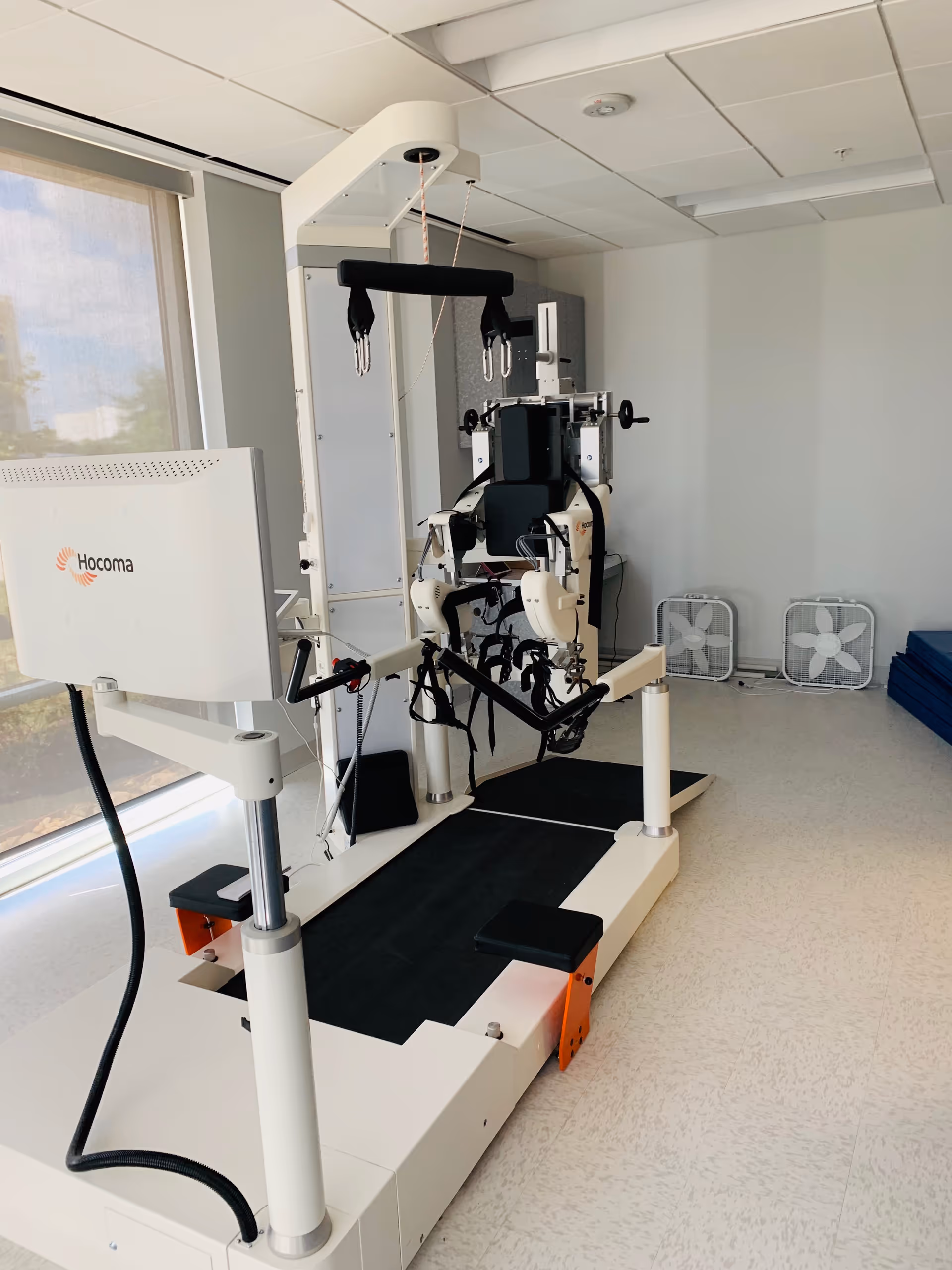 A gait therapy robotic device on a treadmill in a bright medical rehabilitation room.