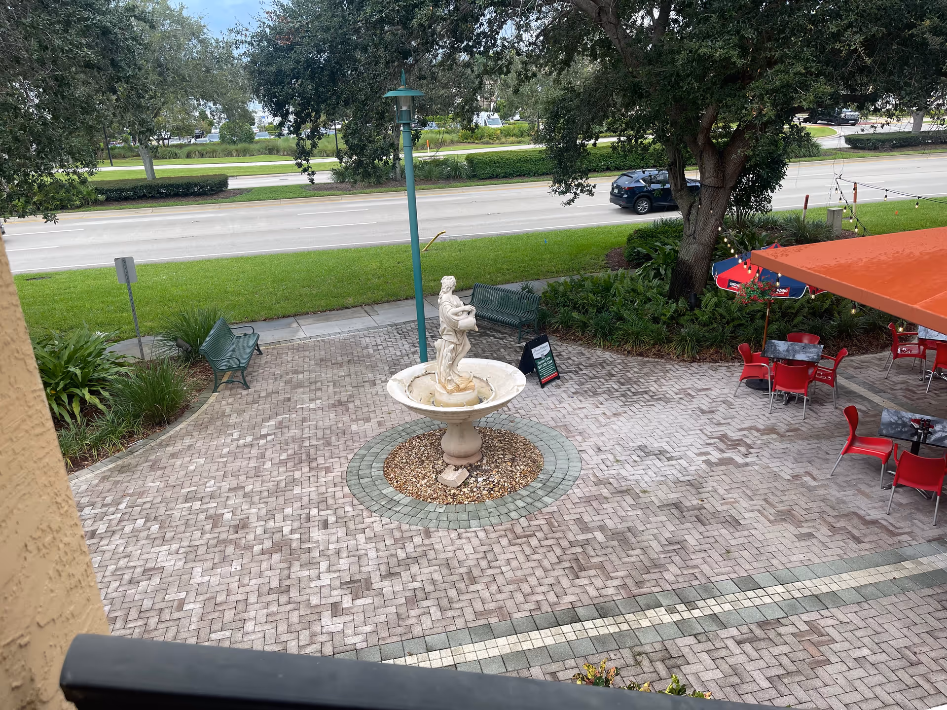 An outdoor courtyard with a central fountain, benches, and red tables under an awning.