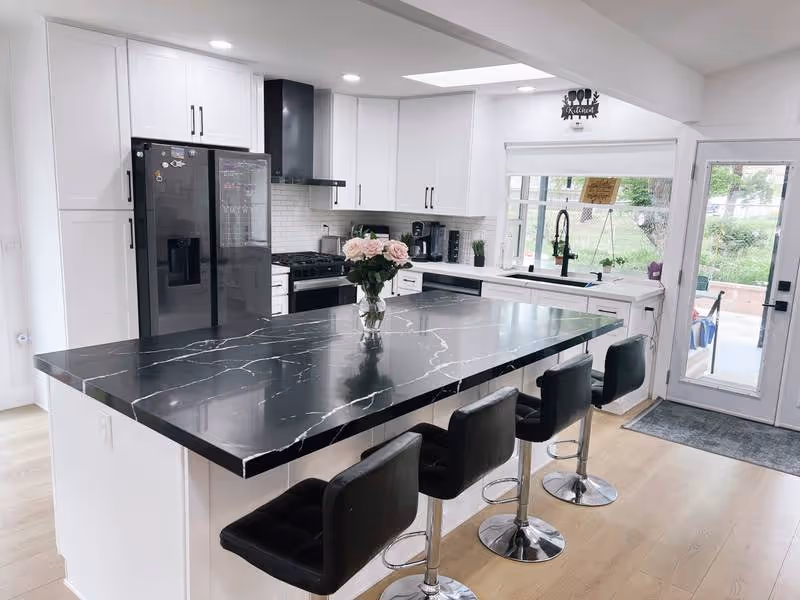 Cristina Home Care kitchen with marble island, white cabinets, and black bar stools.
