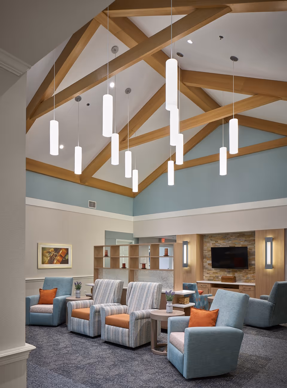 Spacious lounge with blue seating, patterned chairs, tables, and a wood-beamed ceiling.