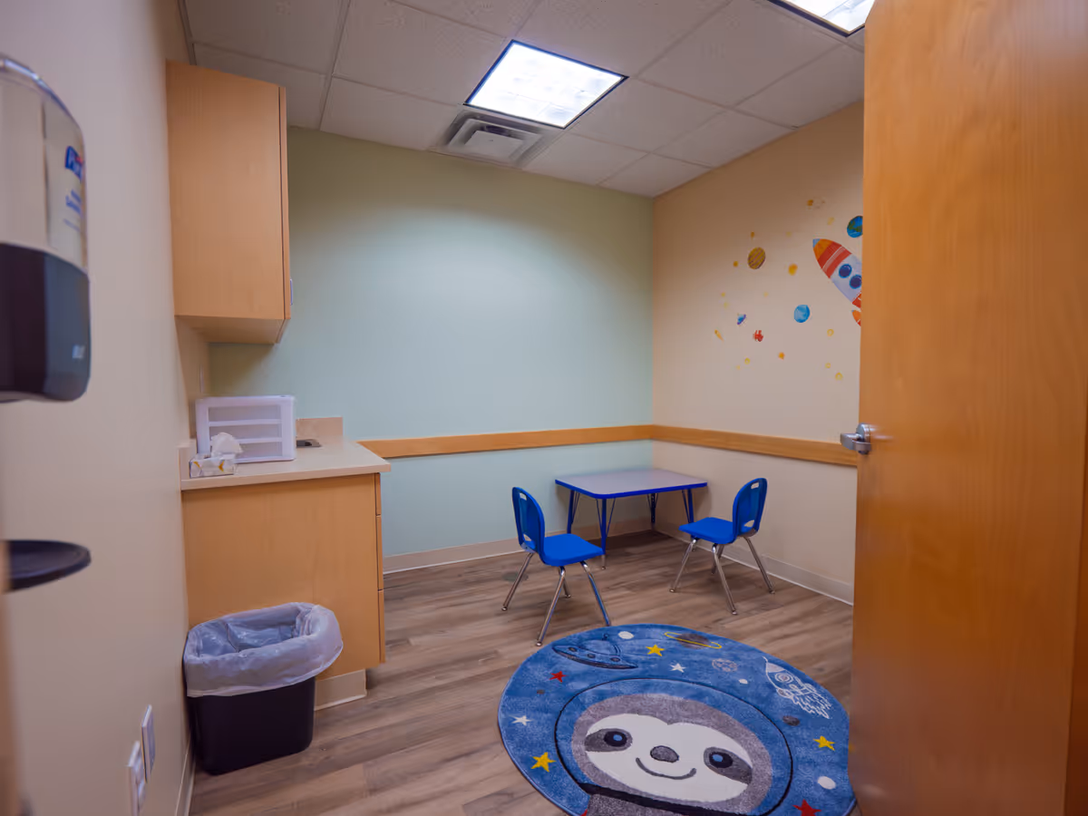 Small, colorful activity room with blue table and chairs, rocket mural.