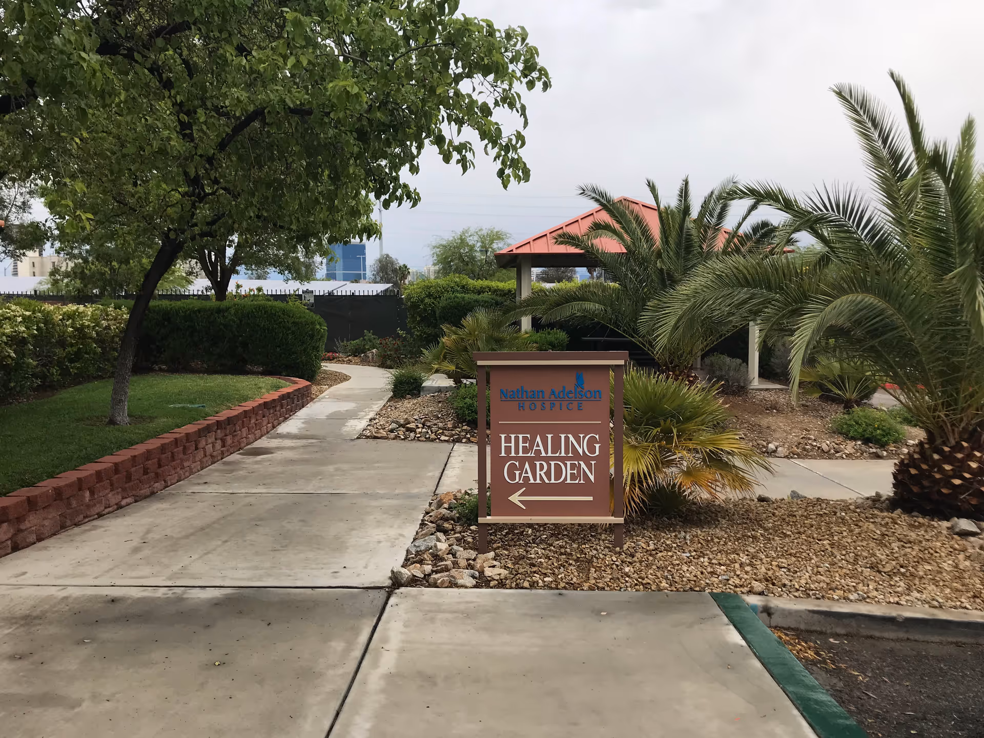 Outdoor pathway with palm trees leads to a Healing Garden sign at the facility.