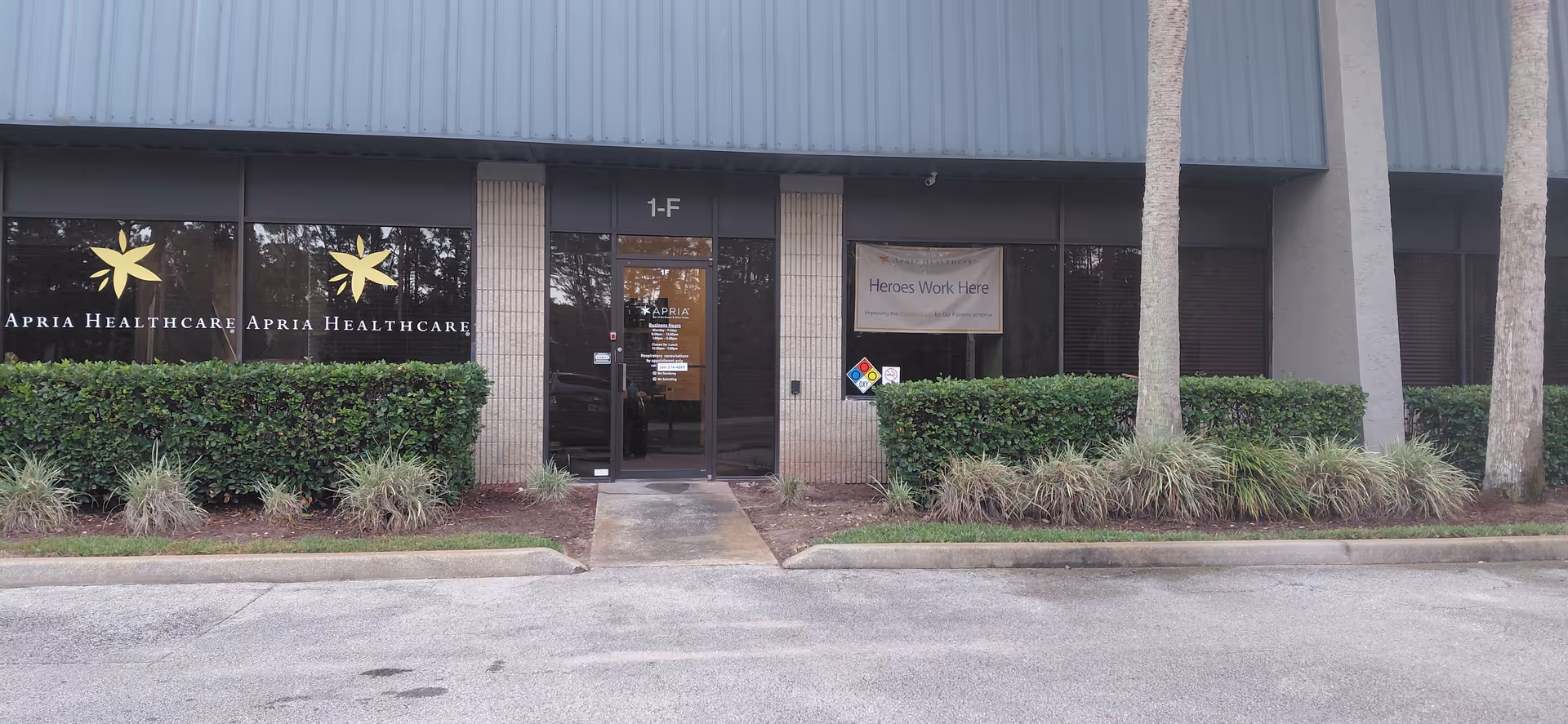 Exterior view of Apria Healthcare building entrance with glass doors and manicured shrubs.