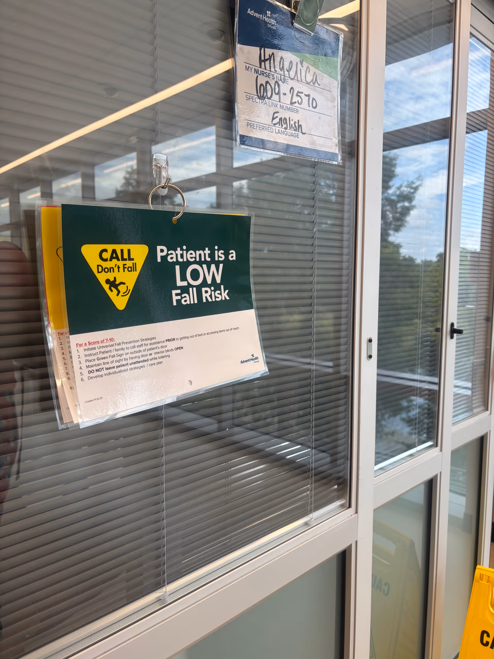 Interior glass corridor with blinds and a hanging sign stating low fall risk.