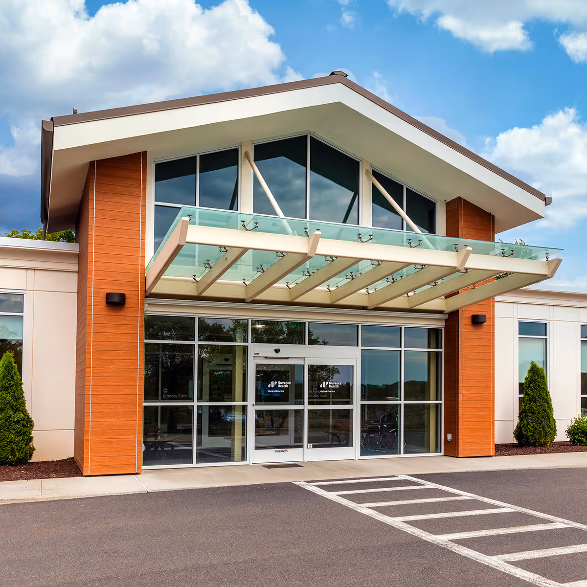 Modern medical practice entrance featuring glass doors, brick columns, and a glass canopy.