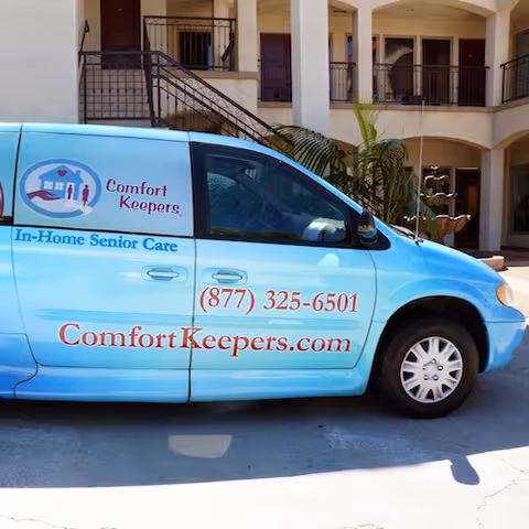 Blue Comfort Keepers van parked outside a two-story building with balconies.